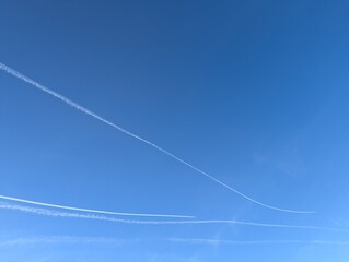 Pattern of contrails from several airplanes travelling east against a clear blue sky