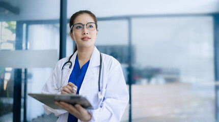 Doctor woman using digital tablet standing in clinic look at camera, Doctor woman wearing glasses and medical coat working in hospital, Healthcare professional service at modern center. 