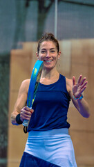 Portrait of a happy female padel player smiling and waving to the camera on an indoor court after the match.