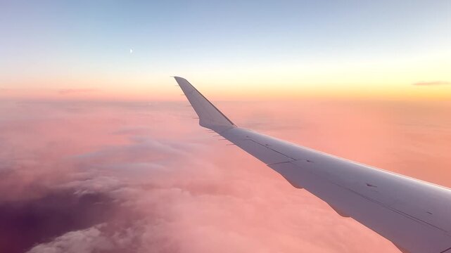 View shows the wing of an airplane extending over a thick layer of clouds on a clear day. The sky appears bright with some clouds visible in the distance.