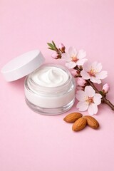 Glass jar of cream with white lid, surrounded by sprig of blossoming and almonds on pink background. Beauty product in transparent container. Cream butter moisturizing with almond oil. Vertical