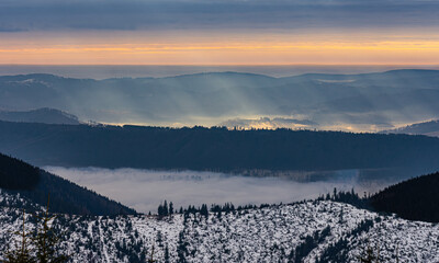Snowy mountain range at sunrise with fog in valleys.