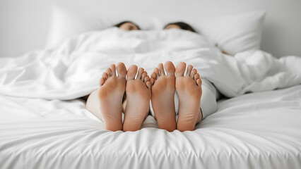 Close-up view of a couple in bed feet peeking out from under the white duvet, relaxed morning mood.