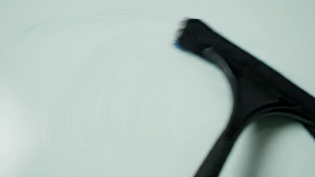 Close-up of a black squeegee cleaning a white surface.