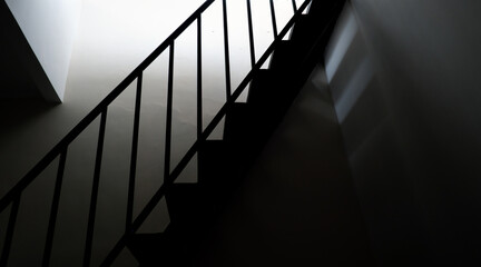 Low-angle silhouette of a staircase with a modern metal railing against a bright light source. The high-contrast composition emphasizes the geometric lines of the steps and the handrail 