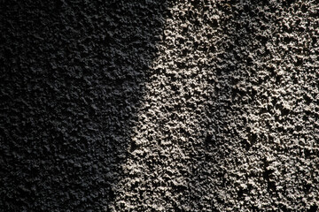 Rough stucco wall illuminated by sunlight casting diagonal grid shadows. The high-contrast light accentuates the deep granular texture of the concrete surface, creating a geometric abstract patter