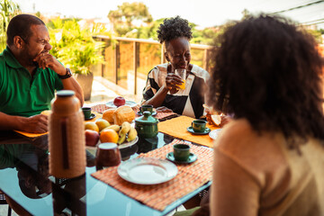 Joyful Black family or friends enjoying a delicious outdoor breakfast with fresh food and drinks on a sunny morning.