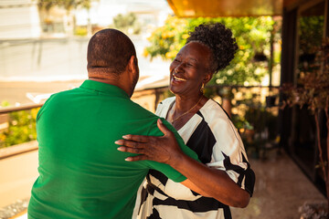 Happy senior African American woman embracing a man, showing joy and affection outdoors on a sunny day.