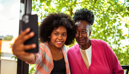 Happy African American grandmother and granddaughter taking a selfie outdoors with a smartphone.