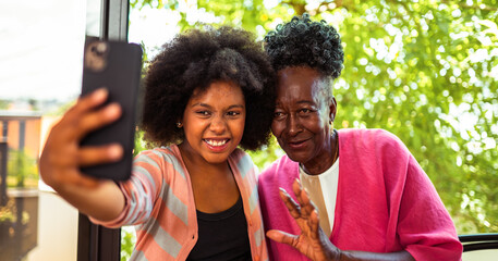 Happy African American grandmother and granddaughter taking a joyful selfie outdoors with a smartphone, sharing a moment of connection and modern technology.