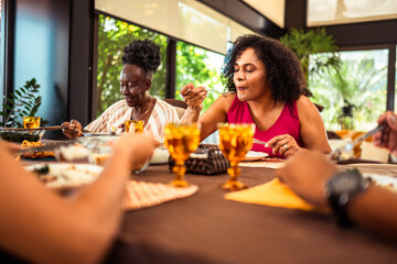 Two African American women enjoy a delicious meal together at a bright dining table, sharing food and conversation in a relaxed home environment.