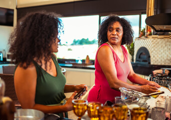 Two Black women engaging in conversation while one washes dishes in a contemporary kitchen setting.