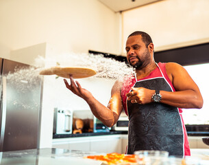 Happy man skillfully tossing pizza dough in a bright, modern kitchen, creating a cloud of flour.