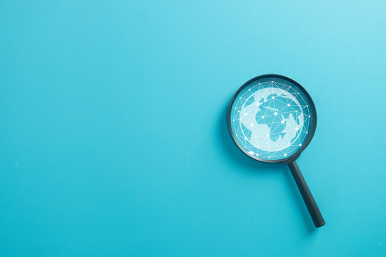 Magnifying glass with digital globe and network connection inside. Concept of global search, internet technology, finding data, analyzing worldwide communication, and discovery on blue background. - Powered by Adobe