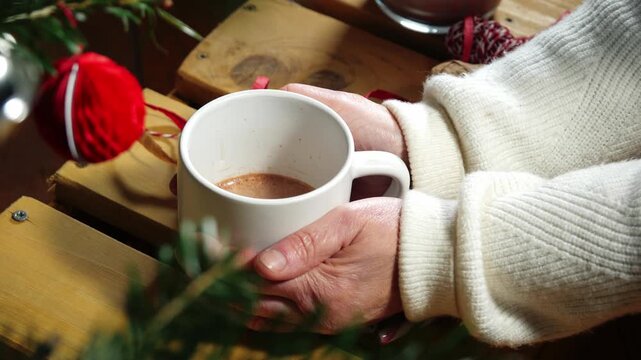 Hands holding mug of hot chocolate through view of Christmas tree