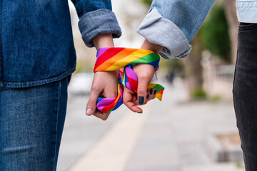 Two people holding hands, wearing rainbow-patterned scarves. The scarf is a symbol of the rainbow pride movement, representing love and acceptance for the LGBTQ community.