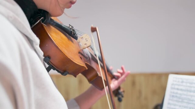Close-up of conservatory-level violin student practicing with sheet music. Focused expression and refined bow movement highlight advanced musical literacy and dedication to classical music education.
