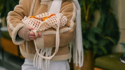 Person holding a reusable mesh bag filled with fresh oranges in winter clothing