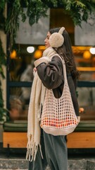 Woman wearing earmuffs and scarf, carrying a mesh bag with oranges, winter street style