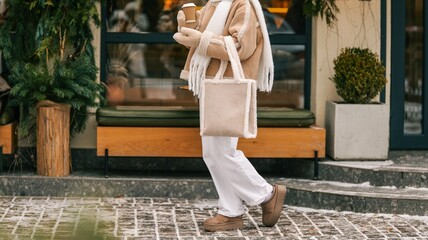 Woman in cozy winter fashion holding a coffee cup and a shearling tote bag