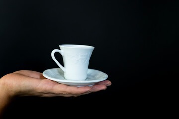A white cup and saucer are being held by a person