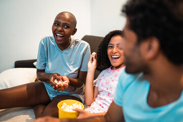 Diverse group of happy friends laughing and eating popcorn during a movie night at home.