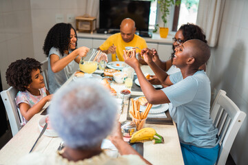 Happy multi-generational Black family enjoying a healthy breakfast together at home, sharing food and laughing during a weekend morning meal.