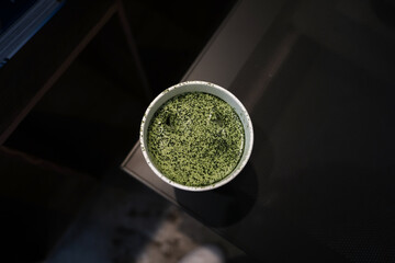 Iced matcha latte with milk foam in a white paper glass.