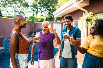Happy multi-ethnic group of friends and family toasting with beer glasses by a swimming pool at a backyard party.