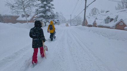 Two snowboarders walk along the snow-covered road leading through ski resort town in Japan. Snowboarders weather the snowstorm returning from the slopes of Niseko, walking through the quiet town.