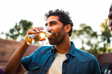 Relaxed Middle Eastern man enjoying a refreshing glass of beer at an outdoor social gathering during golden hour.