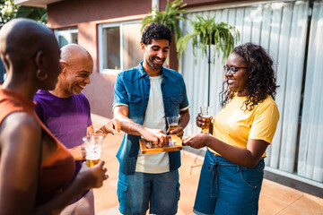 Diverse group of happy friends and family enjoying a backyard party with beer and snacks on a sunny day.