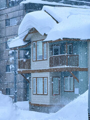 Charming wooden house stands amidst a heavy snowstorm in a ski town. The roof is laden with thick layers of snow, and large icicles hang from the edges. Magical picture of a pure winter wonderland.