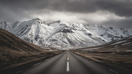 Straight road in Iceland leading toward snow-capped mountains under cloudy sky, winter landscape of nature and adventure, travel and exploration across vast open scenery toward an unknown horizon.