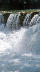 CLOSE UP: Small waterfall with dense jets of crystal clear white water that merge into a swirling pool below, creating abundant white foam and splashes. Raw energy and beauty of a free flowing river.
