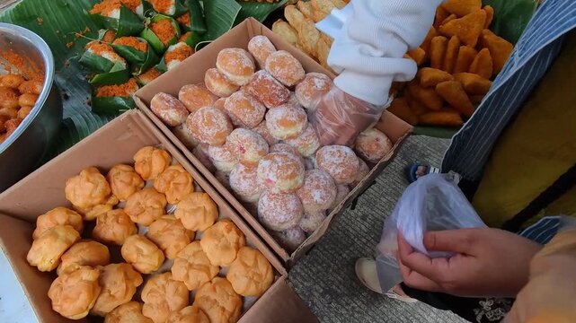 Clip of people picking up donuts with plastic-gloved hands at a dessert buffet. Videography of sweet food being sold at a traditional Indonesian market in 4K HD resolution.
