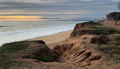 Beautiful sandy beach with red rocks and cliffs. Sunset at dusk with shallow waves on the Atlantic coast in Praia de Loule Velho, Algarve, Portugal