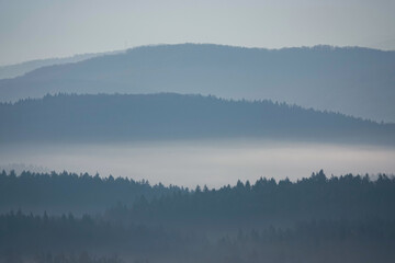 SILHOUETTE: Layered mountain ridges disappearing into winter fog under gentle morning light. The misty atmosphere and subtle tones convey peace and depth in this quiet natural mountain landscape.