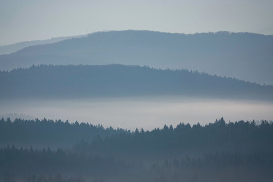 SILHOUETTE: Layered mountain ridges disappearing into winter fog under gentle morning light. The misty atmosphere and subtle tones convey peace and depth in this quiet natural mountain landscape.