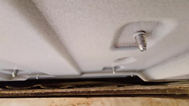 Close-up of metal screws and mounting bolts on the bottom of a white air conditioning unit.