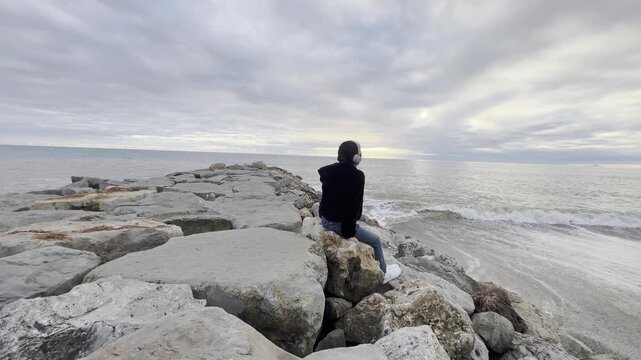 Teenager girl in yellow jacket sitting on a rock and looking at stunning nature background with ocean and cliffs. Travel and tourism. portugal. Dramatic sunset sky. Famous area.
