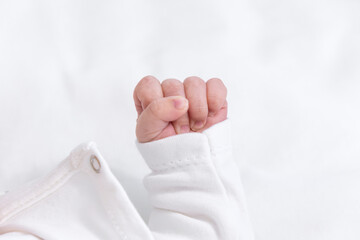 Macro shot of a small infant baby hand with fingers curled into a fist wearing white clothes highlighting skin texture