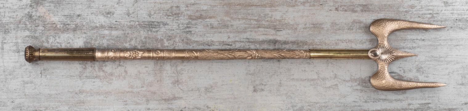 Golden trident medieval weapon on wooden background