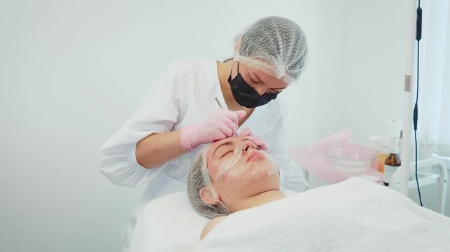 Female cosmetologist removing pus filled pimples from problematic skin of patient. Woman dermatologist treating infected acne on troubled skin of client. Lady cosmetician clearing up pus filled