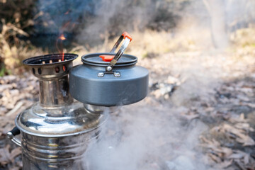 Traditional metal samovar boiling water with a teapot on top and smoke rising during an outdoor picnic in nature