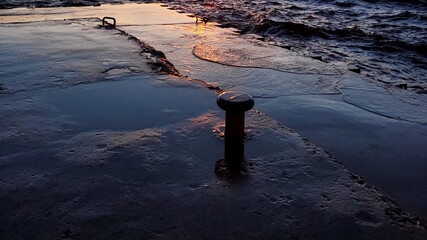 water washing up on pier head at sunset light reflections