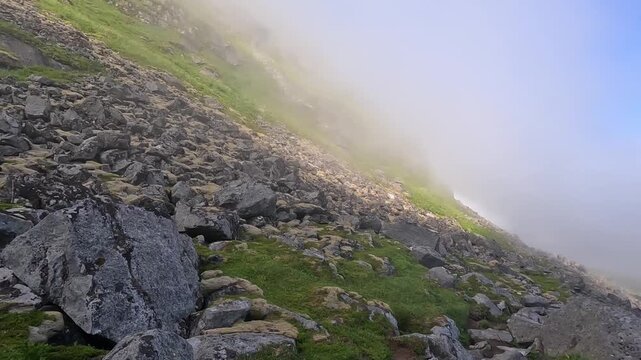 Thick fog blankets alpine hillsides, swallowing the ridgeline and drifting across the valley with low visibility and muted colors.
