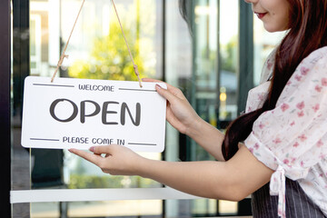 Hands of woman with apron holding the open sign on glass door at cafe. Young owner starting a small business turning open sign. Happy female waitress working in coffee shop with open sign.