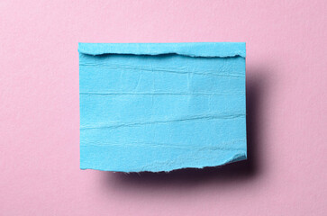 One single blue torn ripped wrinkled crumpled blank paper note with drop shadow, folded edge and copy space for text on pink background