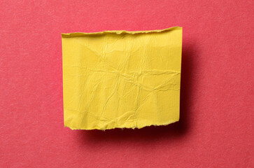One single yellow torn ripped wrinkled crumpled blank paper note with drop shadow, folded edge and copy space for text on red background